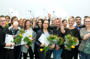 Absolventen der Weiterbildung Leitungsqualifikation halten lachend Ihre Teilnahmezertifikate hoch